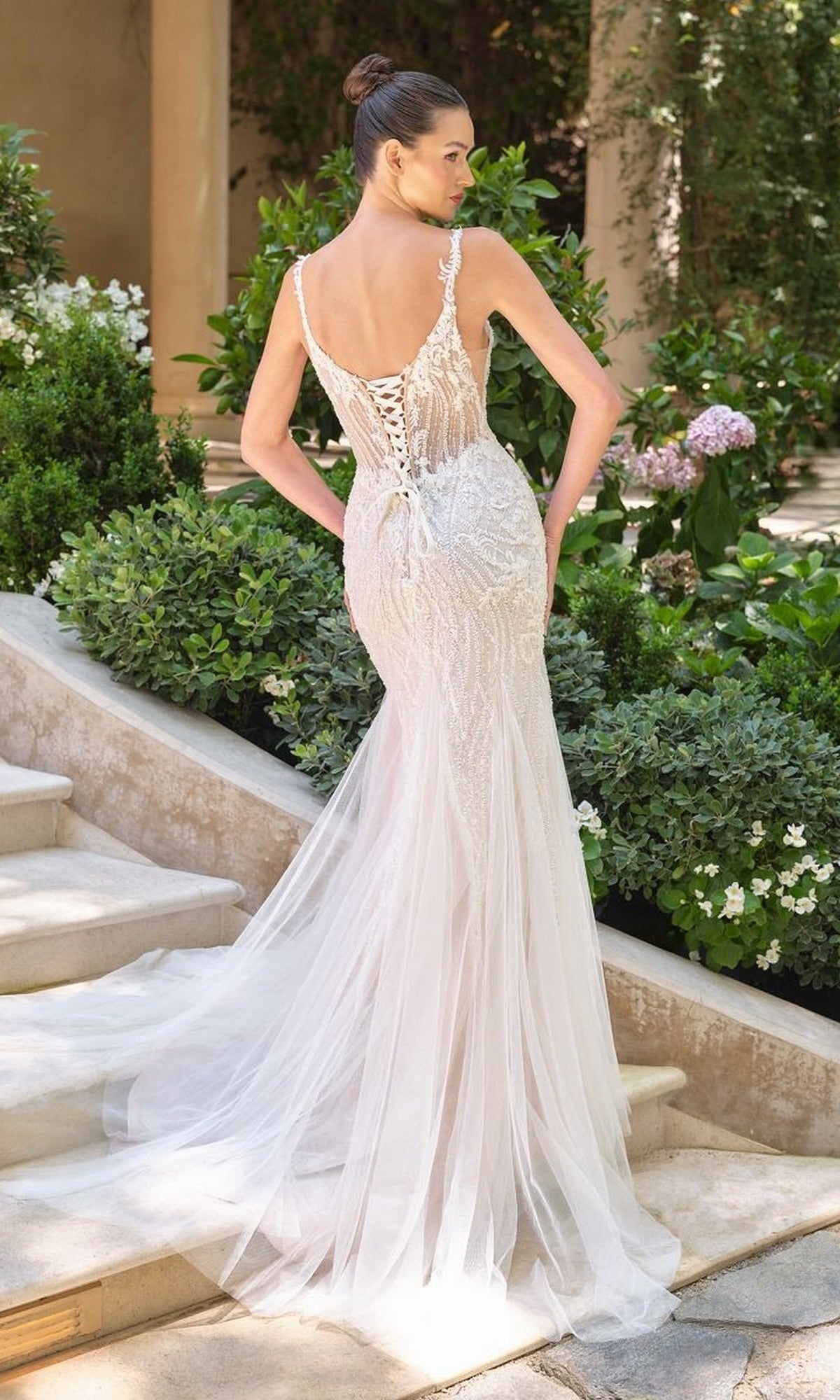 A woman stands on outdoor steps surrounded by greenery, wearing the Andrea and Leo WL066 long wedding dress featuring a fit-and-flare silhouette, beaded embroidery, and a sheer tulle skirt.